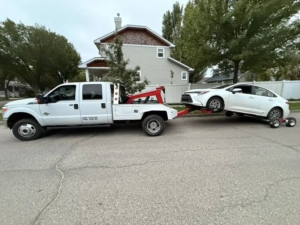 Ironline tow truck towing a white Toyota Corolla on dollies in Edmonton